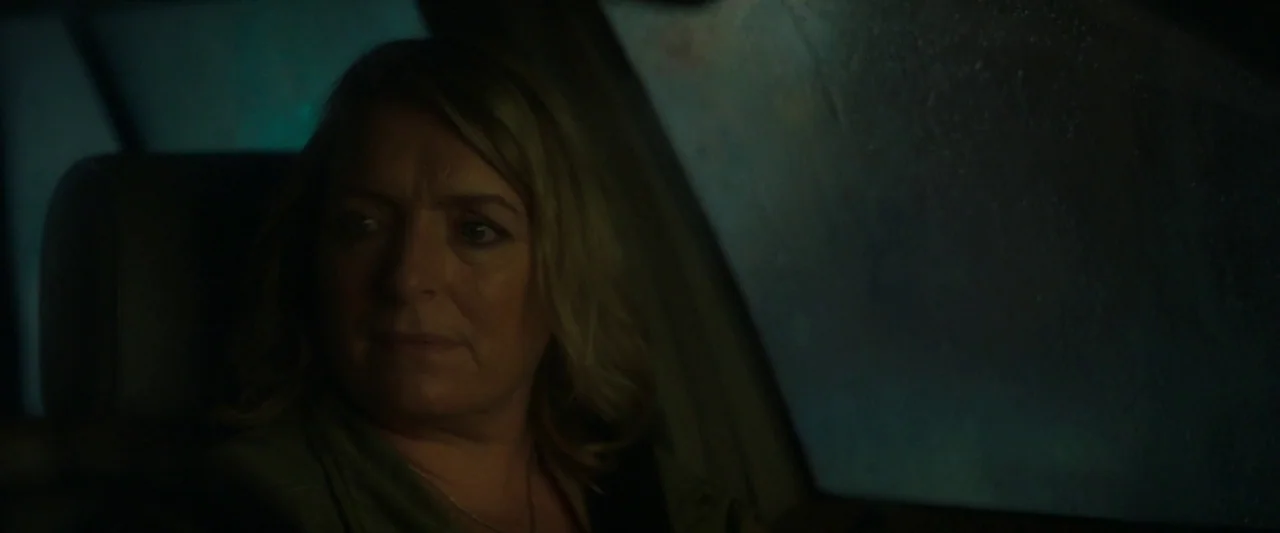 Ali & Ava (2021) movie still: medium — A woman sits inside a car during the night with rain on the window. She gazes out the window at the dark…