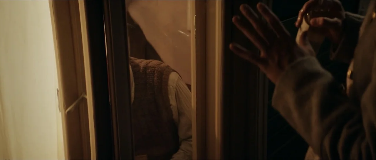 The Rifleman (2019) movie still: medium — A dark indoor hallway with wooden architectural elements and a partially opened wooden door. A person in a…
