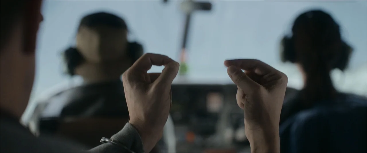 Flight Risk (2025) movie still: closeup — The interior of an aircraft cockpit is visible through the windshield against the sky. A pair of hands in…