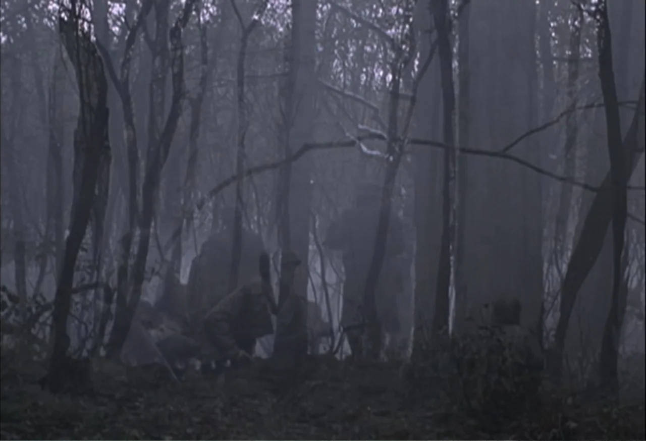 When Trumpets Fade (1998) movie still: wide — A dense woodland filled with thin, bare trees and thick morning fog. Several soldiers in uniform…