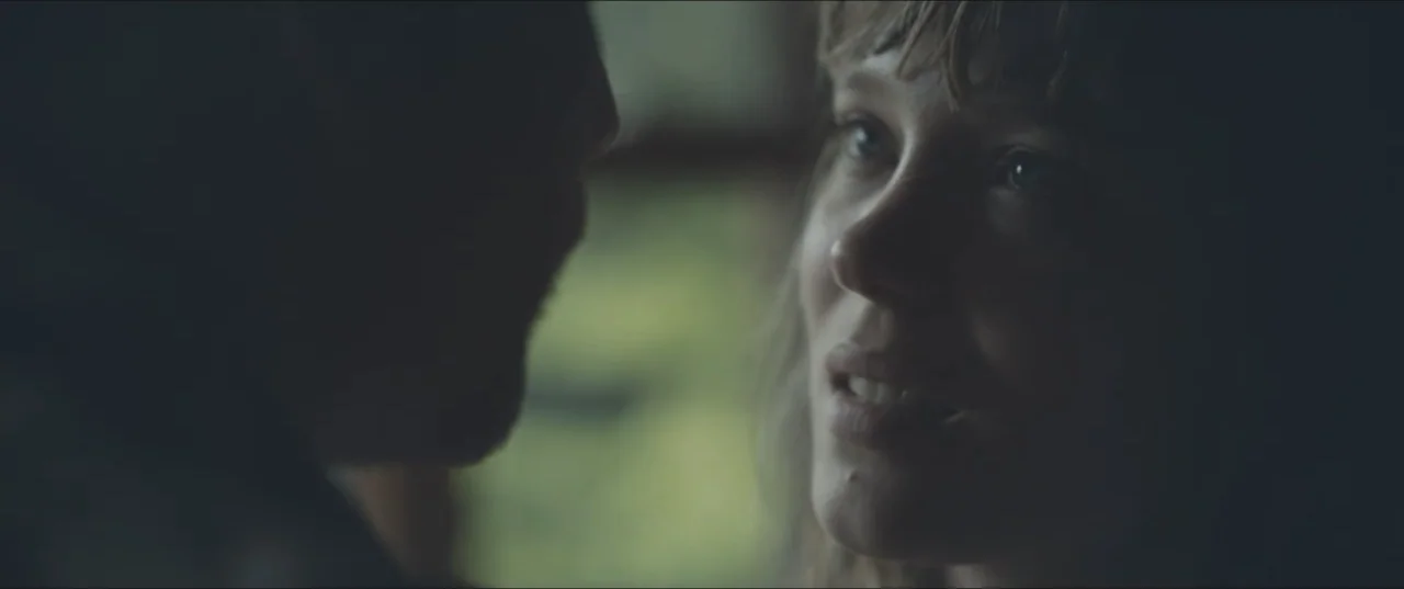 Zoe (2018) movie still: closeup — A dark indoor space contains two people positioned close together facing each other. A woman with light hair and…