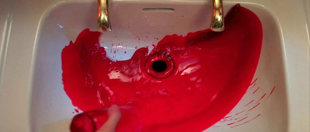 Suspiria (1977) movie still: closeup — A white porcelain washbasin with brass faucets is filled with a bright red liquid. The liquid spirals into…