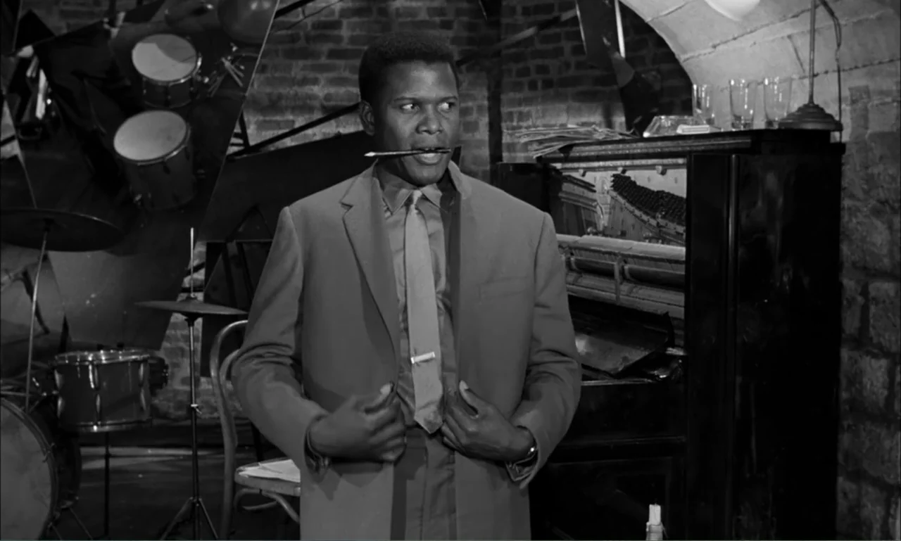 Paris Blues (1961) movie still: medium — A basement music studio with exposed brick walls and an upright piano. A man in a suit adjusts his jacket…