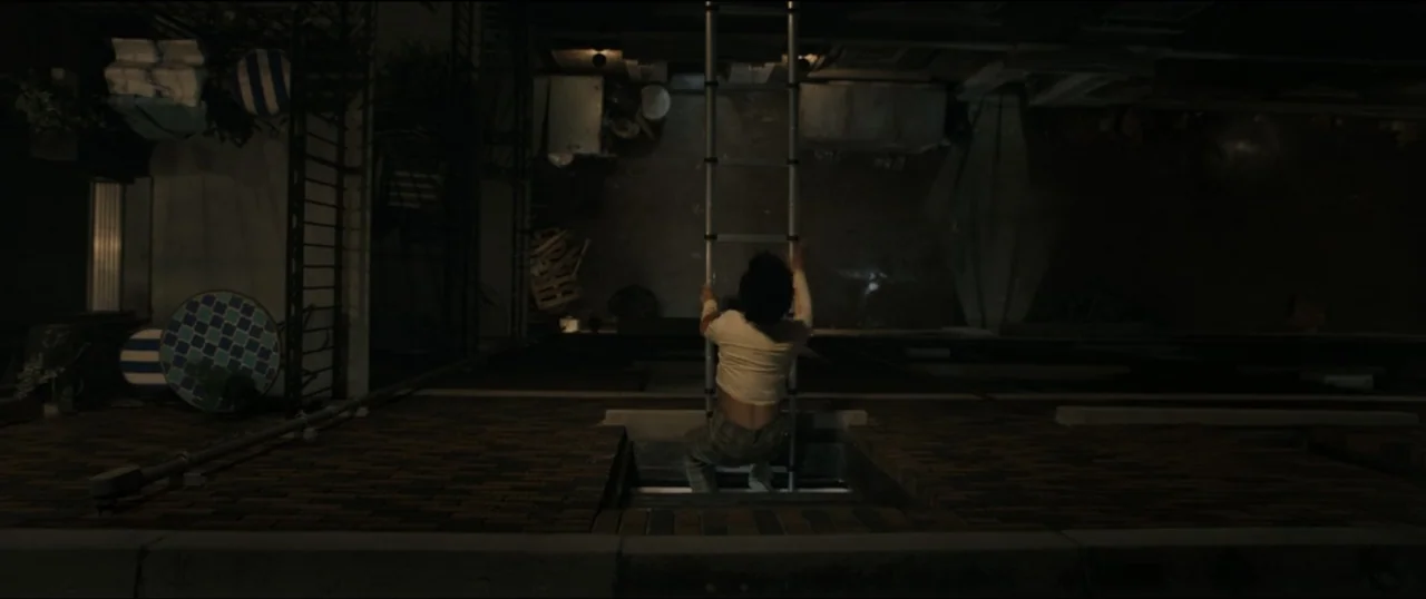 Scream VI (2023) movie still: wide — A dark brick building facade at night features a vertical perspective from above. A person climbs a thin metal…