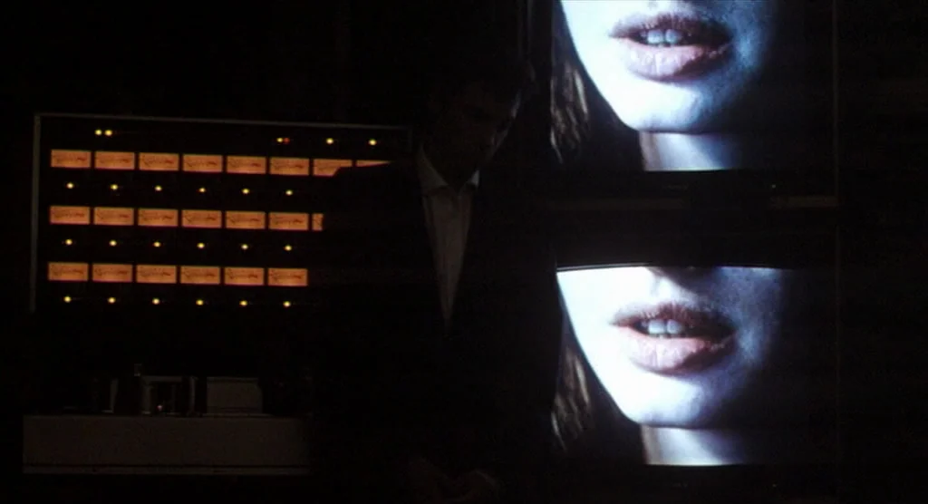 King Lear (1987) movie still: medium — A dark control room features a grid of illuminated electronic displays and video monitors. A man in a suit…
