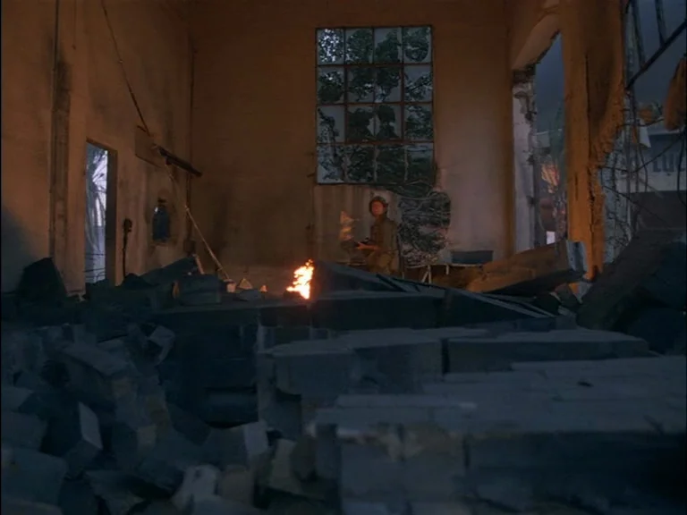 Full Metal Jacket (1987) movie still: wide — A desolate, rubble-filled interior with crumbling walls and a grid-pane window. A lone soldier stands…