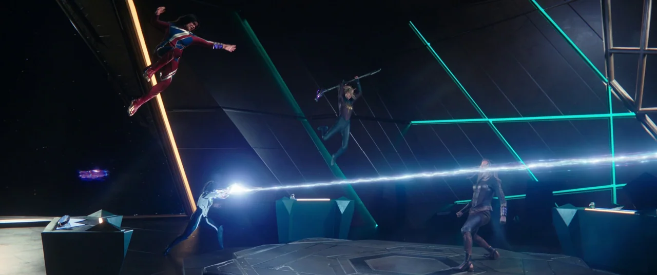 The Marvels (2023) movie still: wide — A dark, angled command center features glowing neon green strips and metallic flooring. Four superpowered…