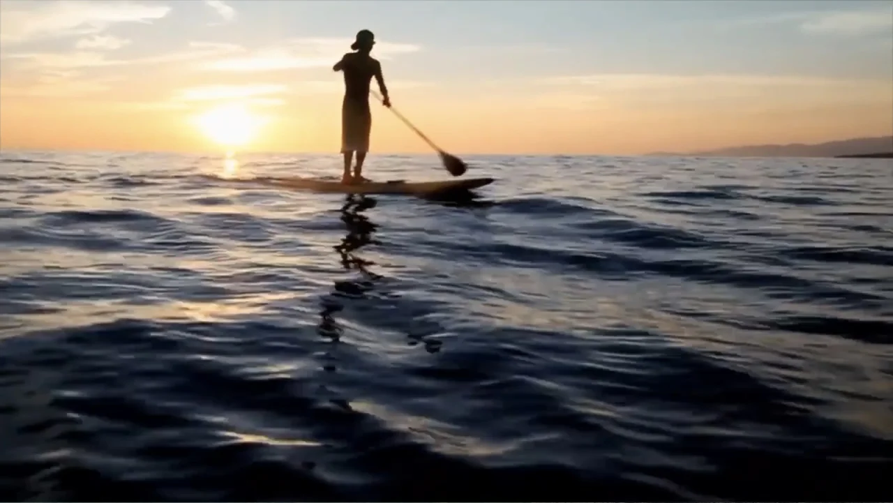 El sueño (2020) movie still: wide — A calm, wide expanse of open water at sunset with a distant horizon line. A lone individual stands on a…