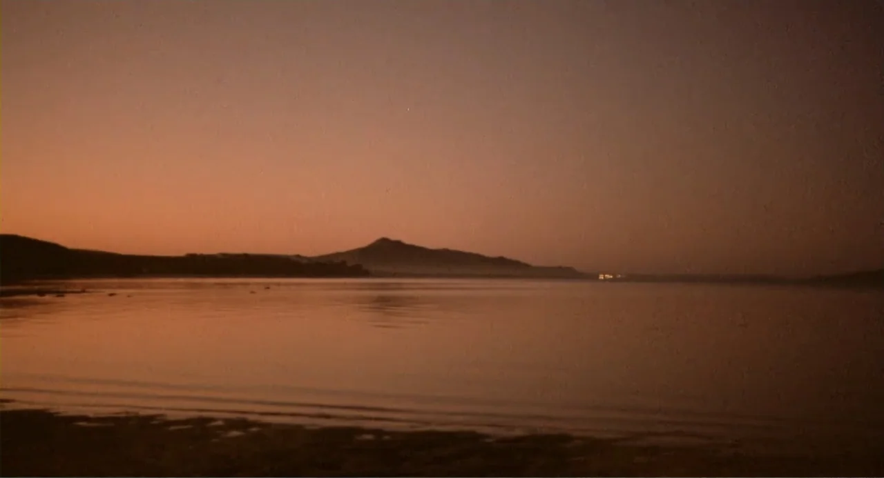 American Ninja 2: The Confrontation (1987) movie still: establishing — A calm lake reflects the muted colors of a sky at late dusk. Low mountains…