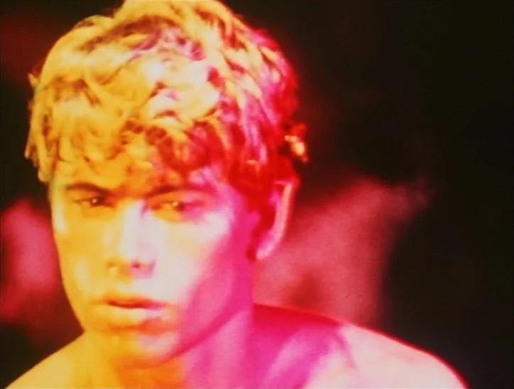 Pink Narcissus (1971) movie still: closeup — A man stands in an indeterminate dark environment with heavy light saturation. Bright red and yellow…