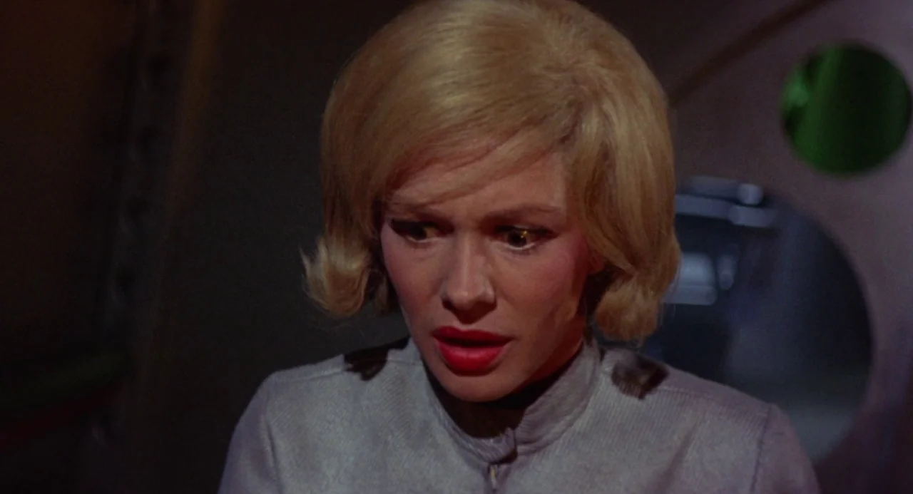 Queen of Blood (1966) movie still: closeup — A close up of a woman inside a metallic vessel with a circular hatch. The woman has platinum blonde…