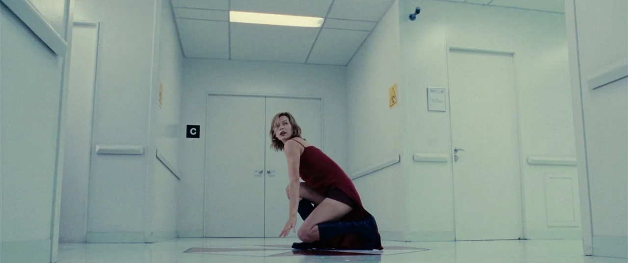Resident Evil: Extinction (2007) movie still: fullbody — A stark white, minimalist laboratory corridor features a central logo on the floor. A woman…