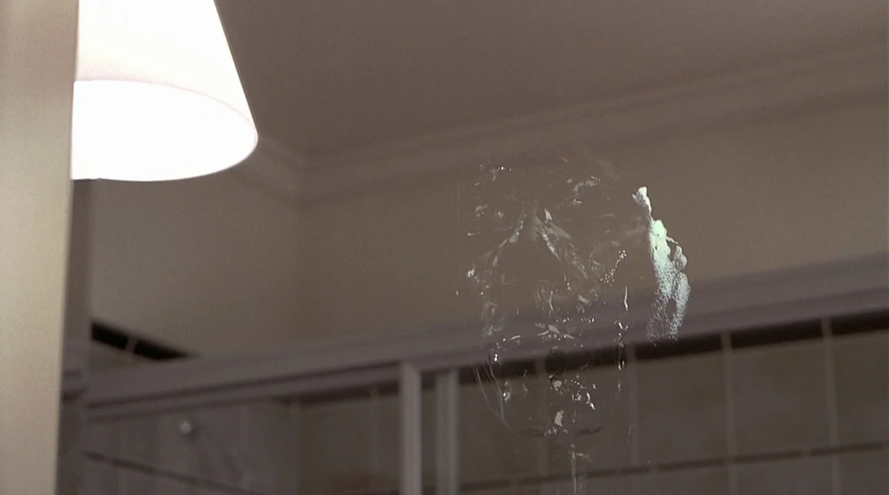 Hollow Man (2000) movie still: closeup — A corner of a modern bathroom with light-colored tiles and a lit wall sconce. A translucent, ghostly…