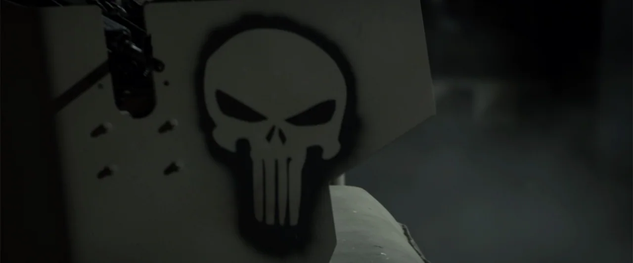 American Sniper (2014) movie still: closeup — A close-up shot of a black skull symbol spray-painted onto a tan, metallic vehicle panel. The…