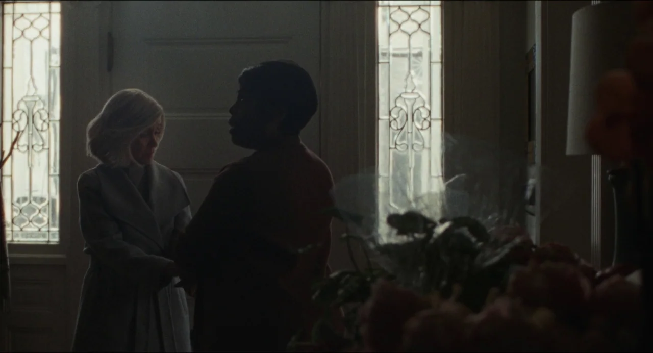 Origin (2023) movie still: medium — A residential entry hall features glass paneled side doors and soft incoming daylight. Two women stand in front…