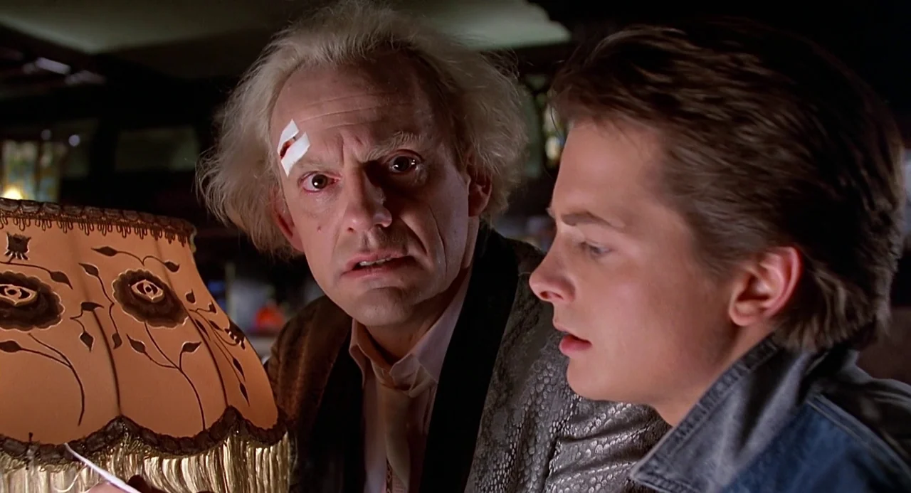 Back to the Future (1985) movie still: medium — A dimly lit room features a patterned table lamp casting a soft golden glow. An older man with wild…