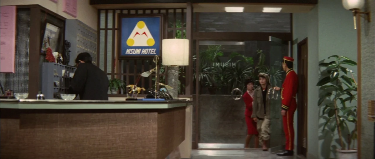 Ghidorah The Three Headed Monster (1964) movie still: wide — A 1960s hotel lobby features wood paneling and a backlit Misumi Hotel logo sign. A…