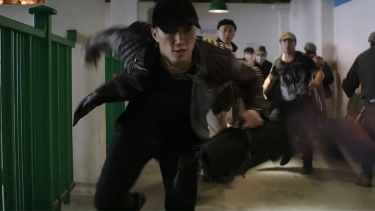 Skyscraper (2018) movie still: medium — An interior hallway with green railings on the left side and white walls. A man in a dark jacket runs…