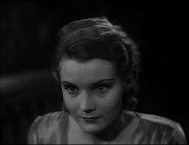 Dracula (1931) movie still: closeup — A dark indoor space with minimal visible background details or architectural features. A woman is centered in…