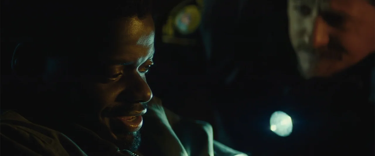 Queen & Slim (2019) movie still: closeup — The interior of a dark police vehicle at night with limited ambient light. A man in the passenger seat is…