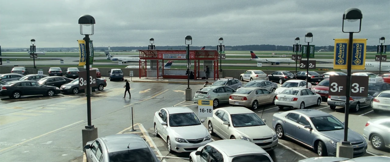 Due Date (2010) movie still: wide — An open-air airport parking facility at Hartsfield-Jackson features numerous parked vehicles under grey skies.…