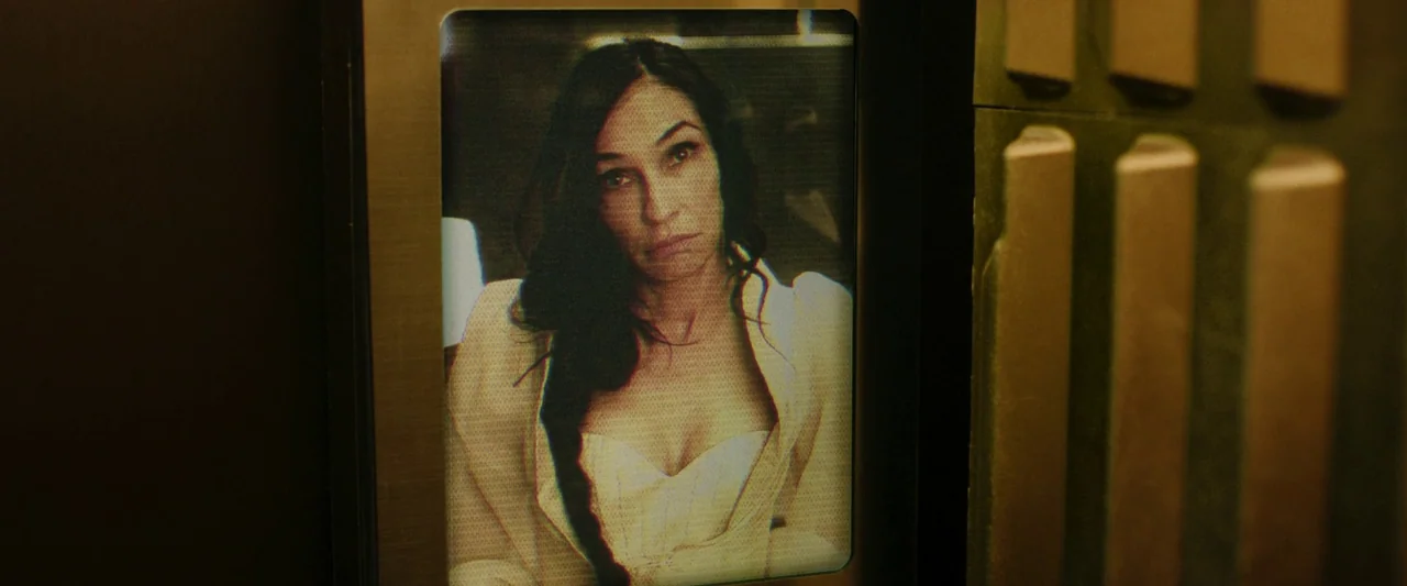 Boy Kills World (2023) movie still: closeup — A woman appears on a small electronic display embedded within an elevator wall. The screen exhibits a…