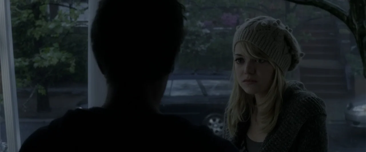 The Amazing Spider-Man (2012) movie still: medium — A residential porch view during an overcast day with a car parked on the street. A woman in a…