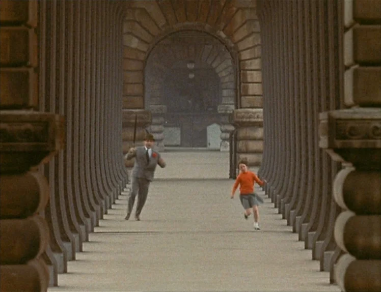 Zazie Dans Le Métro (1960) movie still: wide — A long, repeating stone colonnade features multiple rounded arches and columns in perspective. A man…