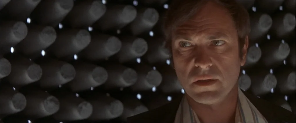 The Man Who Fell To Earth (1976) movie still: closeup — An interior space lined with numerous dark grey acoustic foam cones for sound dampening. A…
