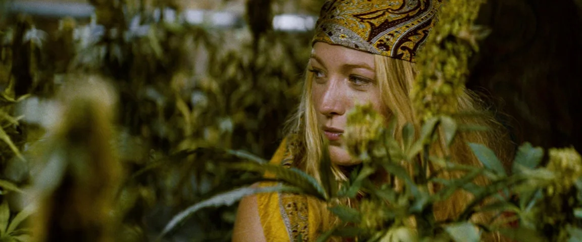 Savages (2012) movie still: medium — A dense outdoor plantation filled with vibrant green cannabis plants in full leaf. A blonde woman in a…