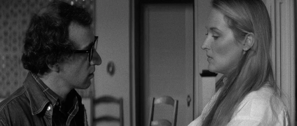 Manhattan (1979) movie still: medium — An interior space features a wooden chair and a doorway in the background. A man wearing glasses and a woman…