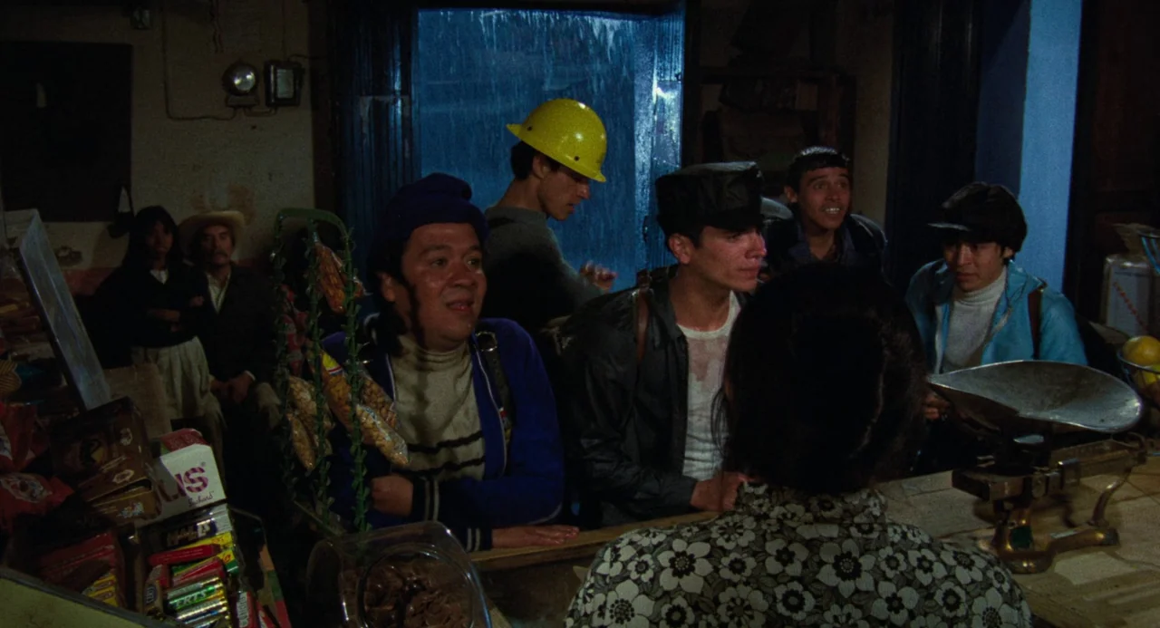 Canoa: A Shameful Memory (1976) movie still: medium — A rustic shop interior with shelves of goods and a metal scale on the counter. Several men…