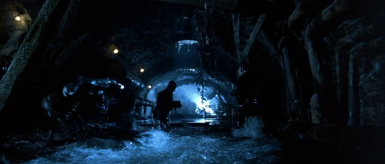 The Rock (1996) movie still: wide — A dark brick-walled sewer tunnel filled with flowing water and thick industrial pipes. Multiple figures in dark…