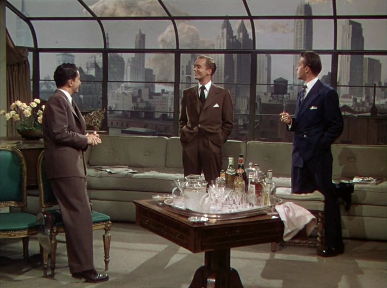 Rope (1948) movie still: wide — A sophisticated apartment with a panoramic window overlooking a painted New York City skyline. Three men in suits…