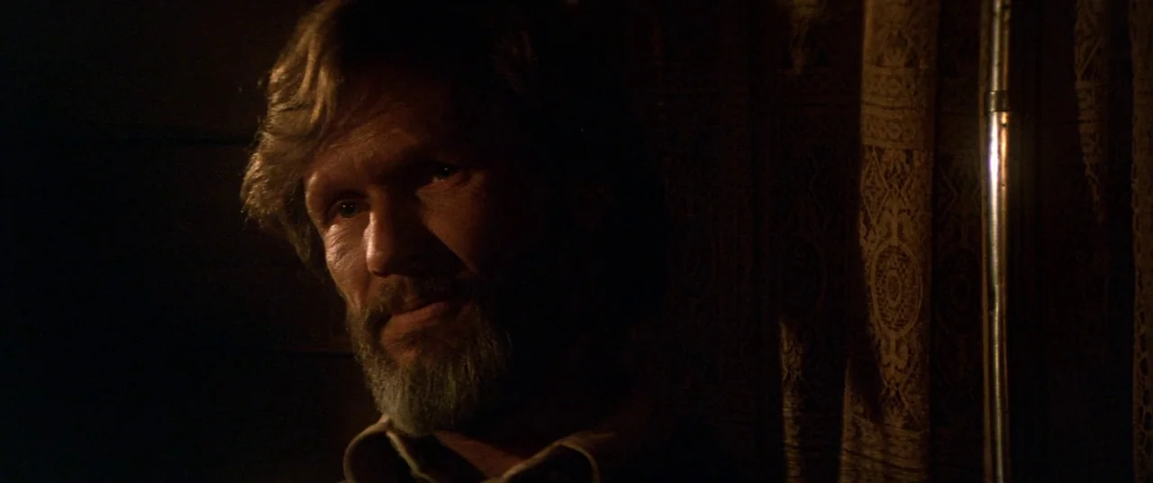 Heaven’s Gate (1980) movie still: closeup — A dimly lit room features a man with a beard partially illuminated by a light source. The background…