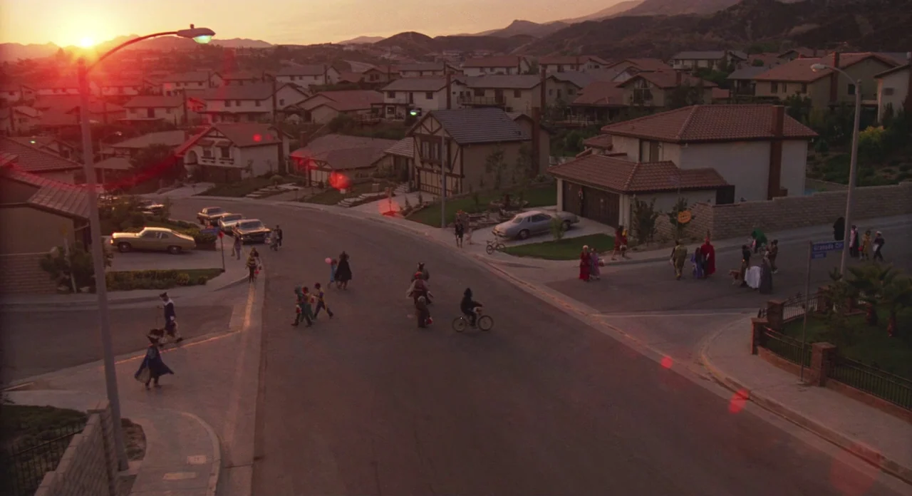 E.T. The Extra-Terrestrial (1982) movie still: establishing — A suburban residential street at sunset features houses and multiple children dressed…