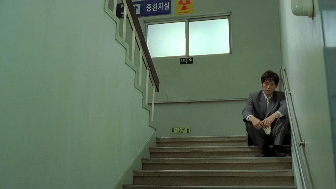 Peppermint Candy (1999) movie still: wide — A quiet concrete stairwell features pale green walls and several informational signs in Korean. A lone…