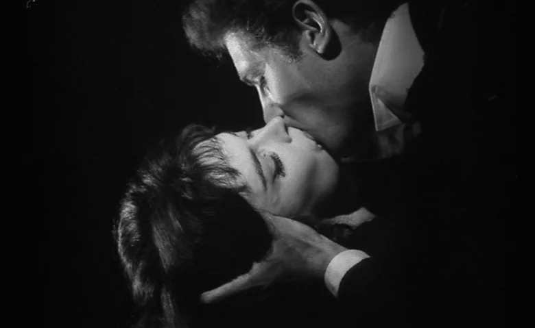 Black Sunday (1960) movie still: closeup — A dark, nondescript environment with no background details visible. A man leans in to kiss a woman whose…
