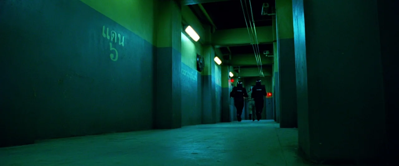 The Hangover Part III (2013) movie still: wide — A long, concrete prison corridor is bathed in artificial green-tinted fluorescent light. Three…
