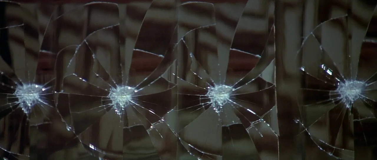 Enter The Dragon (1973) movie still: closeup — A close view of a glass pane featuring four distinct circular spiderweb fracture patterns. The glass…
