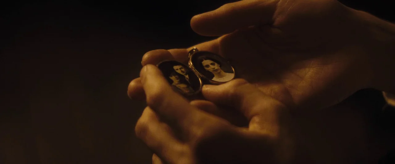 The Immigrant (2013) movie still: closeup — Hands hold open a small, ornate gold locket in a dim, dark environment. The open locket displays two…