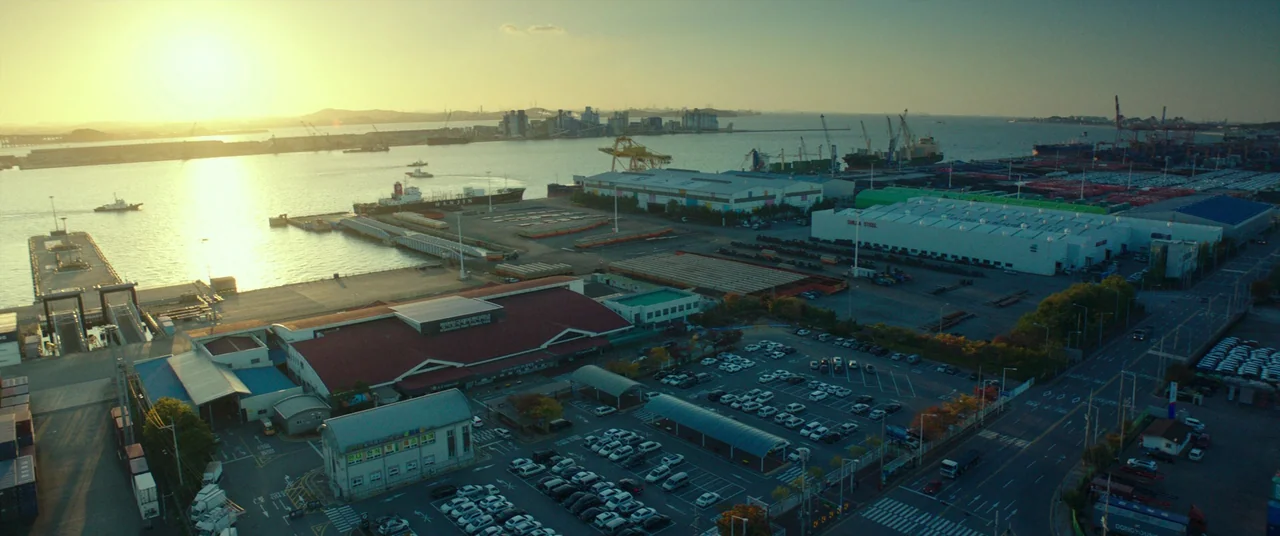 Beasts Clawing At Straws (2020) movie still: establishing — An aerial view of an industrial port features cargo ships and large warehouse…