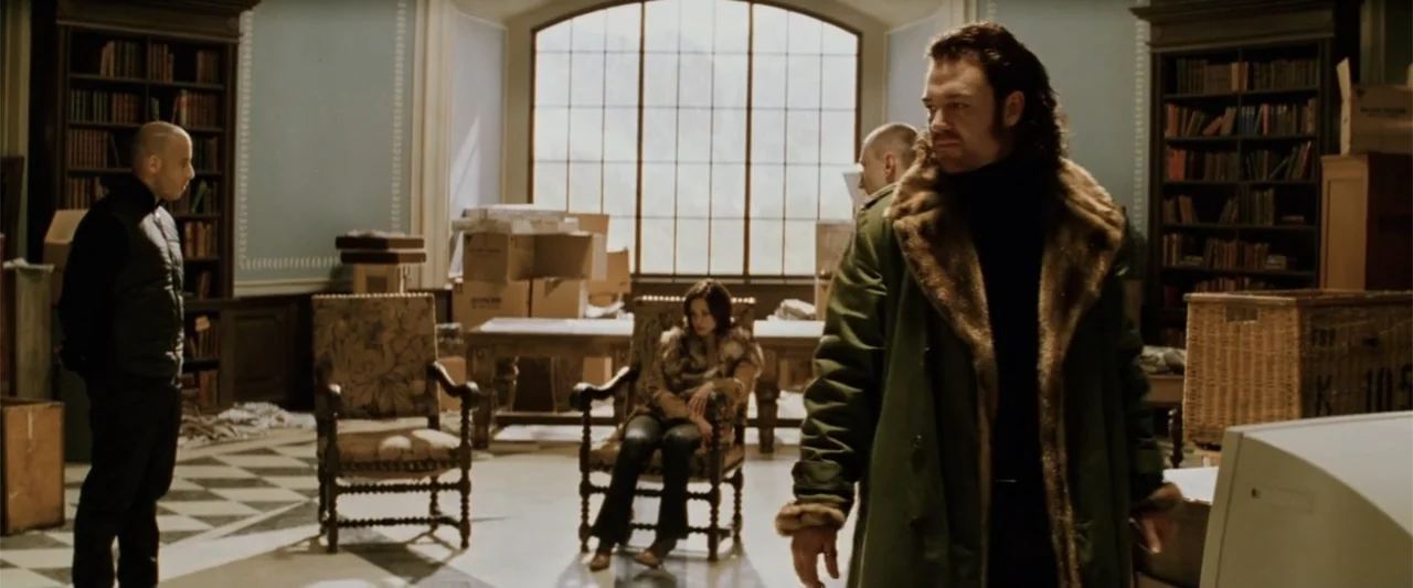 xXx (2002) movie still: wide — A spacious room features blue walls, large arched windows, and checkered tile floors. A man in a heavy coat stands in…