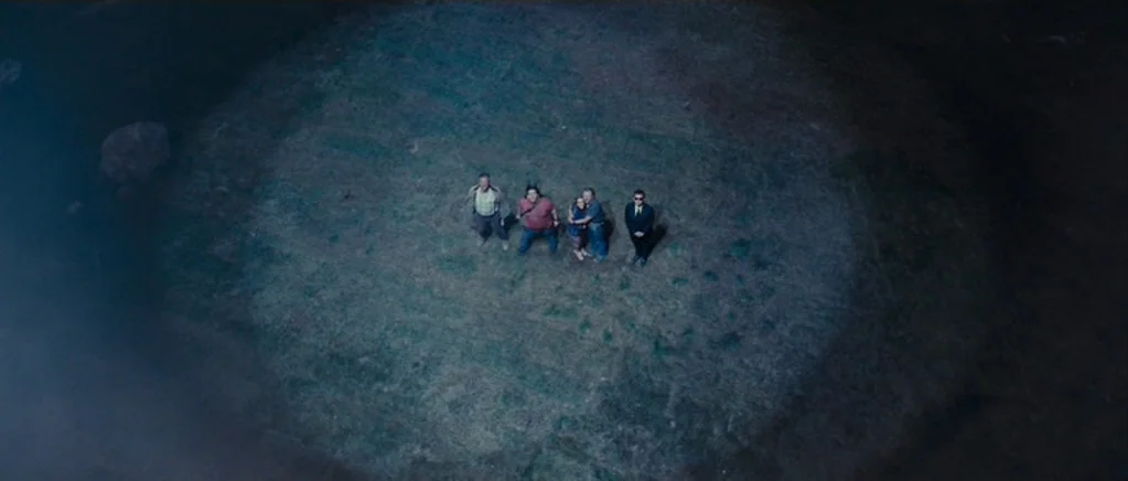 Paul (2011) movie still: wide — A group of five individuals stands within a tight circular spotlight in an open field. They are looking directly…