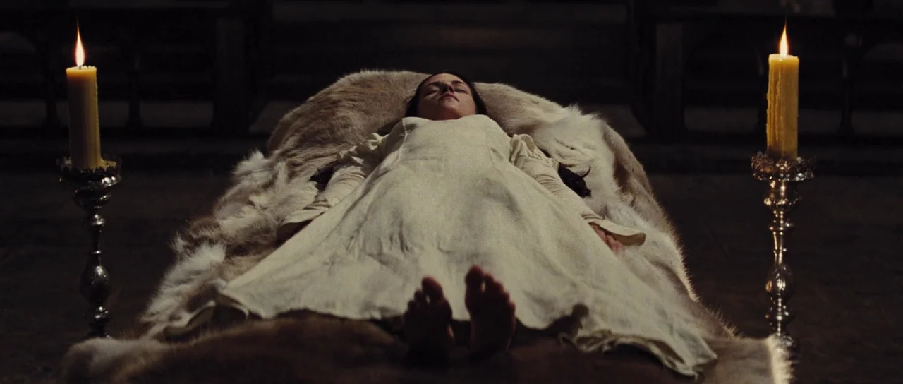 Snow White and The Huntsman (2012) movie still: fullbody — A woman lies on a stone slab covered in thick animal furs within a dark chamber. She…