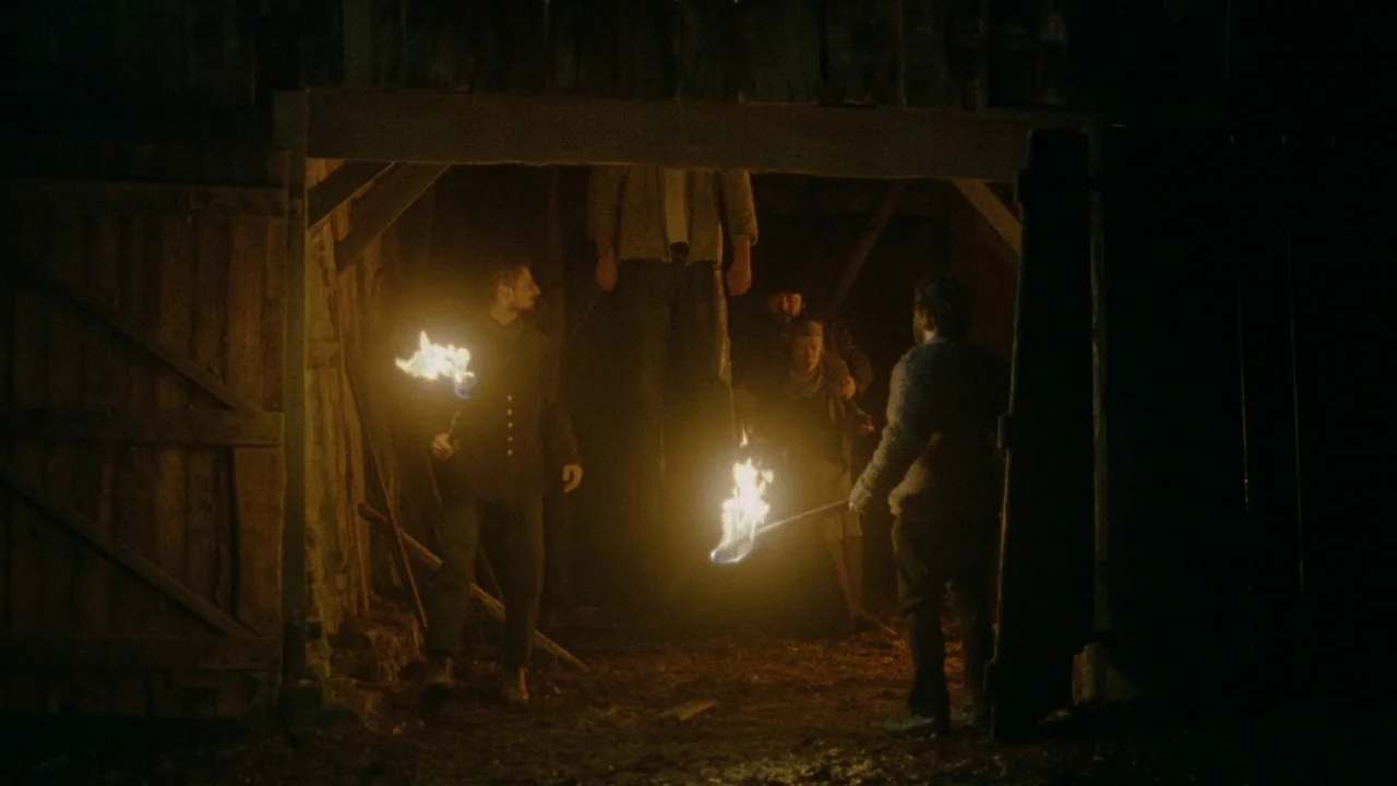 The Devil’s Bath (2024) movie still: fullbody — A group of people standing in a dark, rustic wooden structure at night. The individuals hold flaming…