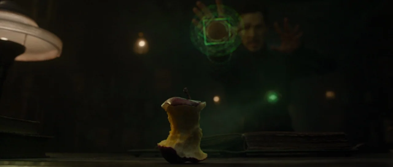 Doctor Strange (2016) movie still: medium — A dimly lit room contains an apple core resting on a flat surface. A man in the background manipulates a…