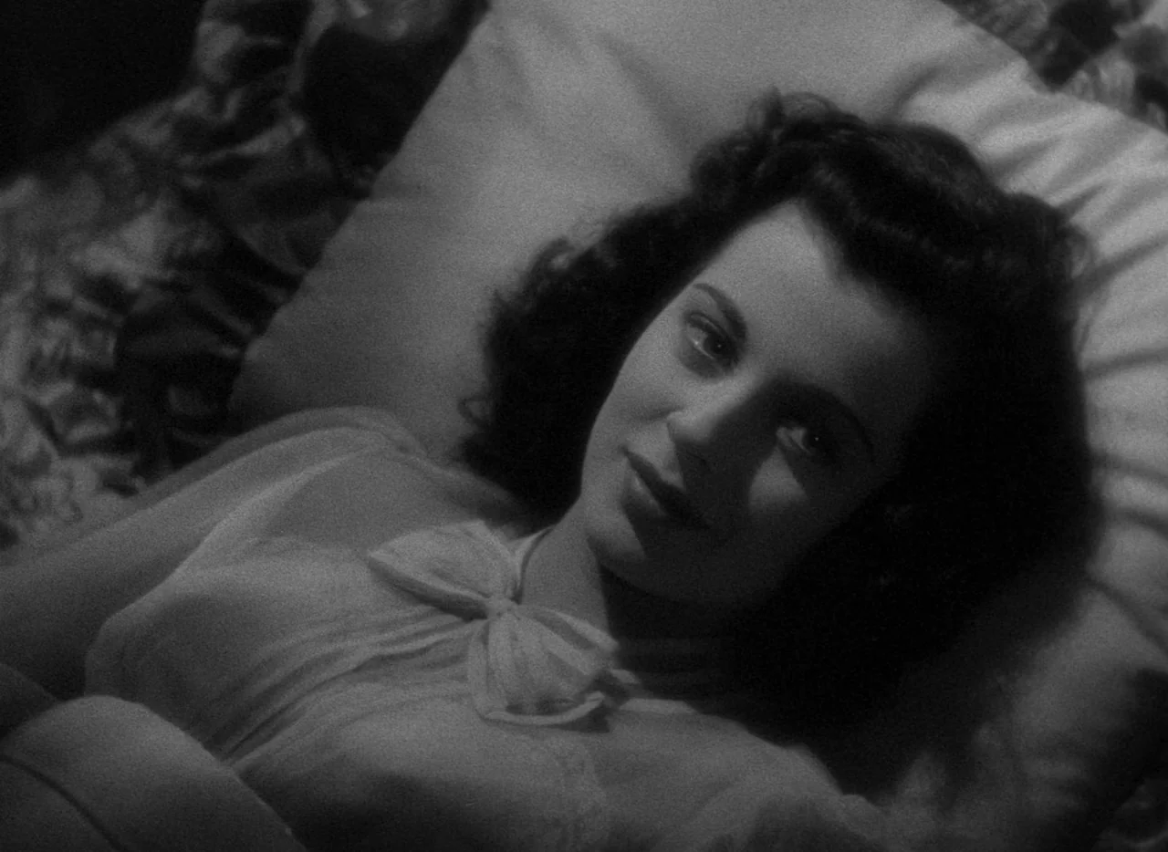 The Uninvited (1944) movie still: closeup — A woman lies on a plush, patterned pillow surface in a dimly lit room. She rests her head back while…