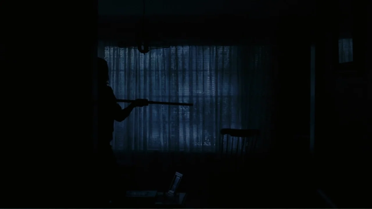 Tomorrow, When the War Began (2010) movie still: medium — A dark living room features a window covered by thin, light-filtering curtains. A…
