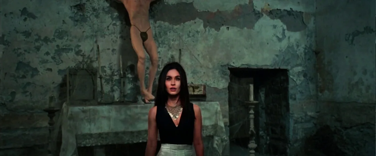 Zeroville (2019) movie still: medium — A dilapidated room features peeling paint on stone walls and an altar. A woman stands in the foreground as a…